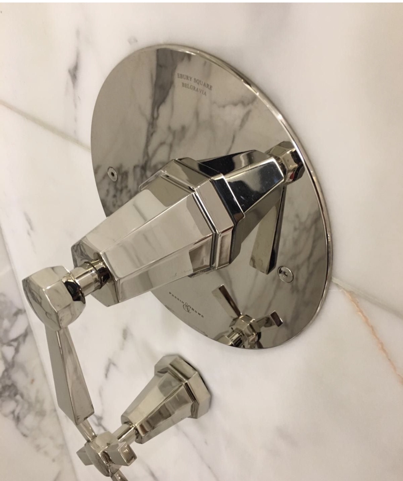 Polished nickel shower controls on white marble
